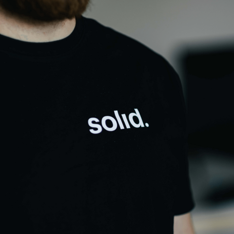 Gros plan sur un t-shirt noir avec le logo 'solid.' blanc, illustrant l'application du branding sur les supports de communication de la firme.