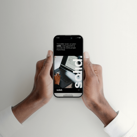 Mains tenant un smartphone affichant le site web mobile de Solid, démontrant l'adaptabilité du design web sur différentes plateformes.