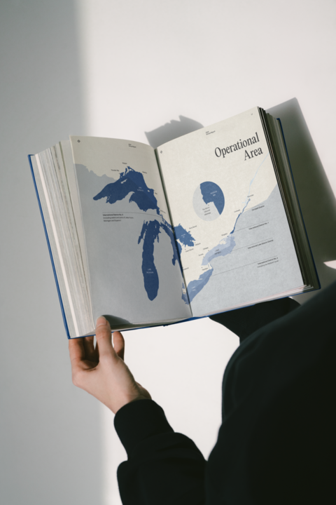 Une personne tient le rapport annuel ouvert, révélant une carte détaillée de la zone opérationnelle des Grands Lacs. L'image met en valeur le design informatif et la qualité de la publication.