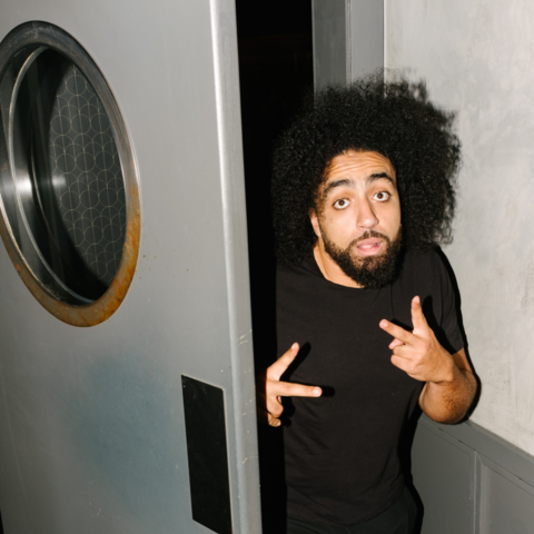 Portrait spontané et plein de caractère d'un humoriste épiant par la lucarne d'une porte de scène, capturant l'essence des coulisses.