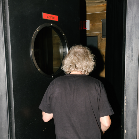 Photo d'ambiance capturée de dos, montrant un humoriste s'apprêtant à franchir la célèbre porte circulaire vers la scène.