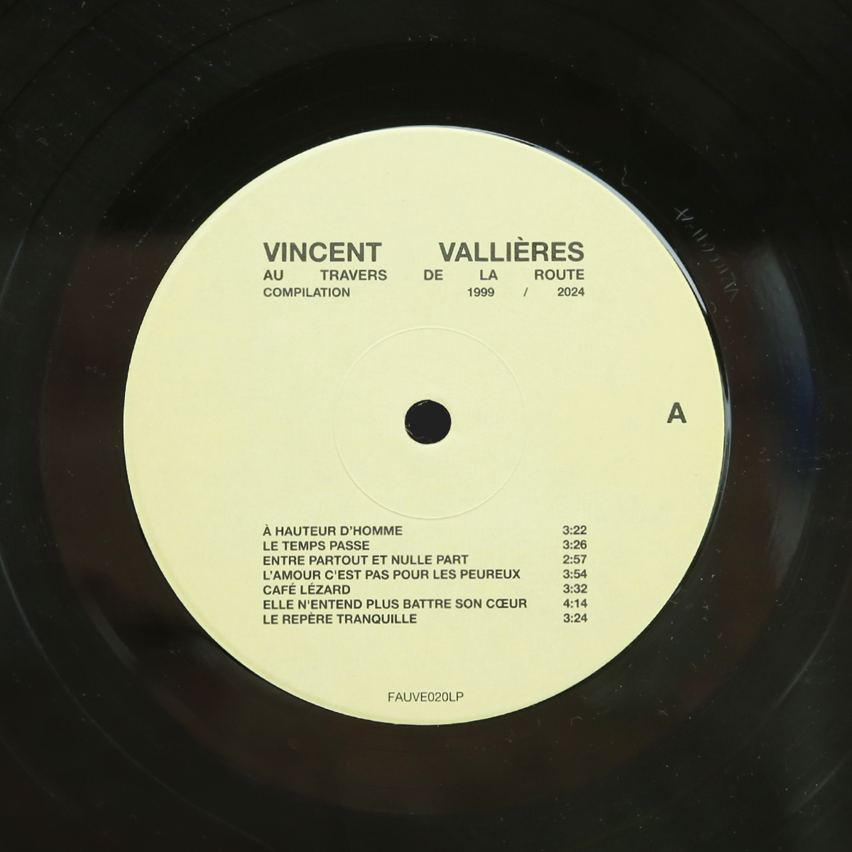 Gros plan centré sur le macaron (l'étiquette) de la Face A du vinyle. On y lit clairement le titre de la compilation et la liste des six premières chansons, dont « À hauteur d'homme » et « Le temps passe ».