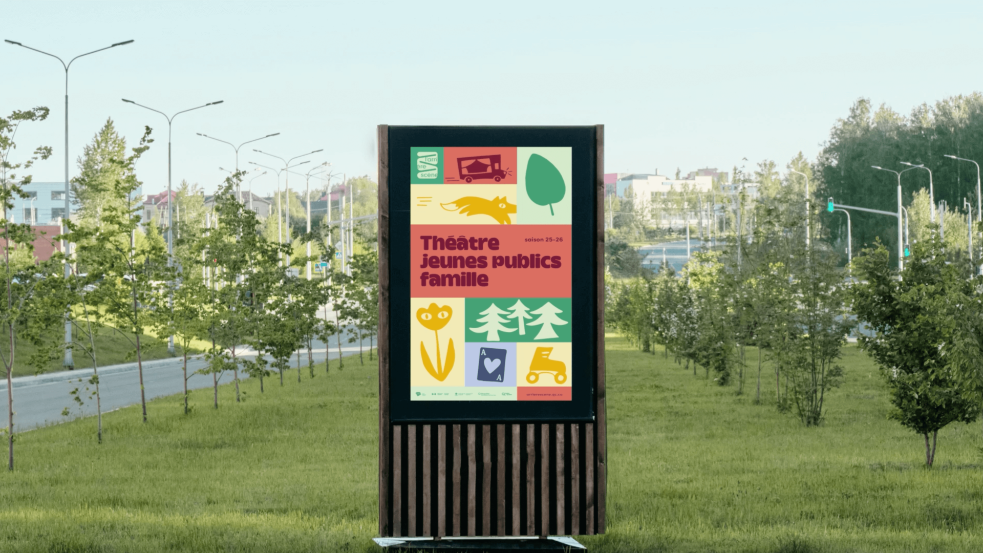 Panneau publicitaire numérique extérieur pour le théâtre jeunes publics famille, situé dans un parc verdoyant. L'affiche présente un design graphique en grille modulaire et colorée, utilisant des pictogrammes et icônes ludiques.